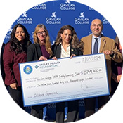 Photo of check presentation which includes representatives from the YMCA of Silicon Valley, Valley Health Foundation of Santa Clara County, Santa Clara County Board Supervisor Sylvia Arenas, and Gavilan College Superintendent President Dr. Pedro Avila.  The group is standing in front of a blue photo backdrop with the Gavilan College hawk logo in white.  